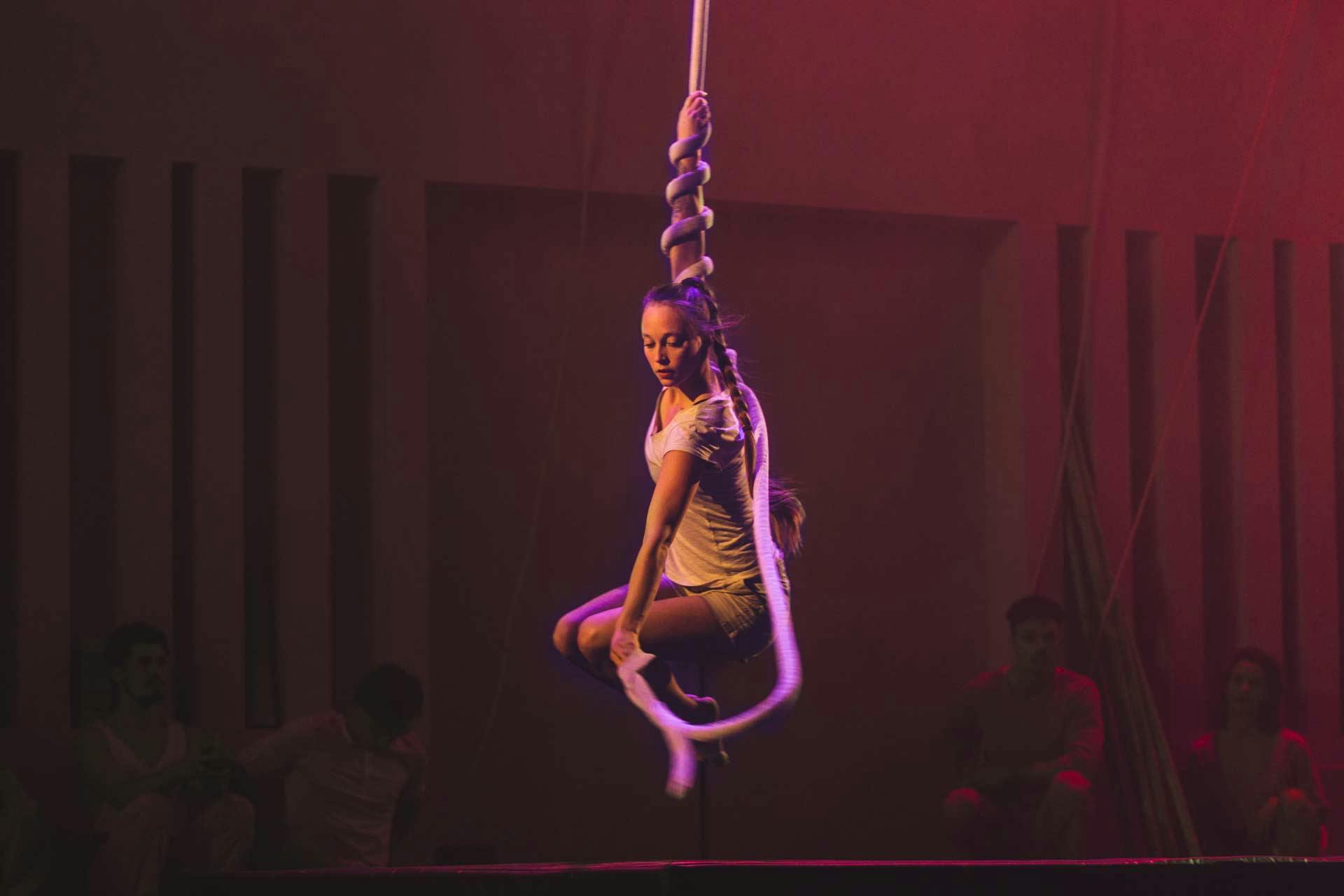 Melinda, during a show, hanging from a rope. The rope is twisted around her arm like a snake